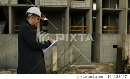 Construction engineer in a hard hat standing and looking at a tall building Construction engineer in a hard hat standing and looking at a tall building 134188437