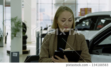 Businesswoman checking her new car in a modern showroom Businesswoman checking her new car in a modern showroom 134188563