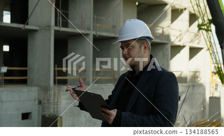 Engineer in hard hat checking his watch while holding a tablet on site 134188565