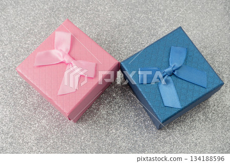 Two small boxes with ribbons are placed on a shiny surface. One box is blue and the other is pink. These boxes are ready for gifting during a party or event. Two small boxes with ribbons are placed on a shiny surface. One box is blue and the other is pink. These boxes are ready for gifting during a party or event. 134188596