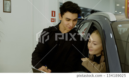 Couple and salesman looking at new car in a bright showroom Couple and salesman looking at new car in a bright showroom 134189025