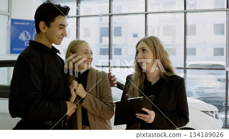 Salesman and female client discussing car in a showroom Salesman and female client discussing car in a showroom 134189026