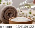 Pouring essential oil drop into wooden bowl of white bath salts for aromatherapy spa treatment 134189122
