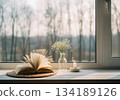 Serene windowsill scene with open book, lit candle, and delicate baby breath flowers. 134189126