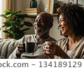 Mature african american couple laughing and enjoying coffee together on a cozy living room couch. 134189129