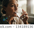 Close up of a mature woman drinking refreshing water from a glass for hydration and wellness. 134189136