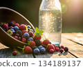Freshly picked mixed berries spilling from a rustic wooden bowl next to sparkling water at sunset. 134189137