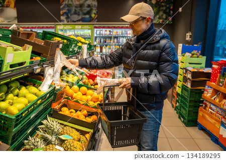Man tearing off a plastic produce bag at a fresh fruit and vegetable section in a supermarket. Raises awareness about single use plastic consumption in daily grocery shopping. Man tearing off a plastic produce bag at a fresh fruit and vegetable section in a supermarket. Raises awareness about single use plastic consumption in daily grocery shopping. 134189295