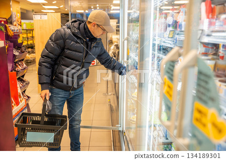 Man choosing dairy products from a refrigerated shelf in a supermarket. Highlights daily shopping routine and conscious selection of milk and fermented food. Man choosing dairy products from a refrigerated shelf in a supermarket. Highlights daily shopping routine and conscious selection of milk and fermented food. 134189301