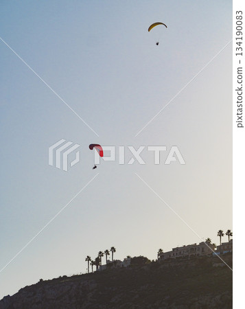 Paragliders flying in blue sky. 134190083