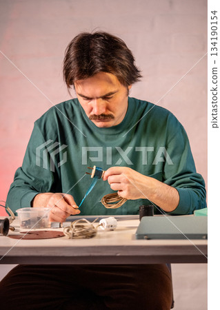 Crafter working at workshop renovating vintage lamp, removing sticky tape wrapped around plug. Crafter working at workshop renovating vintage lamp, removing sticky tape wrapped around plug. 134190154