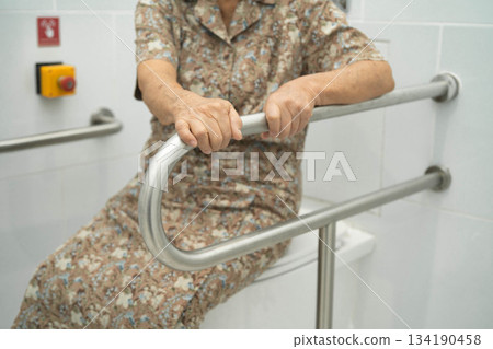 Asian elderly woman patient use toilet support rail in bathroom. Asian elderly woman patient use toilet support rail in bathroom. 134190458