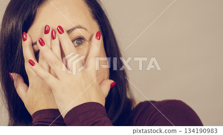 Woman peeking through her hands 134190983