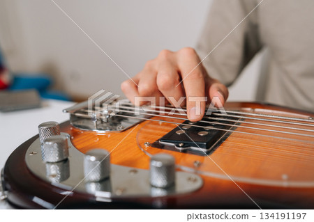 Close-up of musician hand plucking and adjusting bass guitar strings, preparing and tuning instrument for practice, rehearsal or live performance with focused precision. Close-up of musician hand plucking and adjusting bass guitar strings, preparing and tuning instrument for practice, rehearsal or live performance with focused precision. 134191197