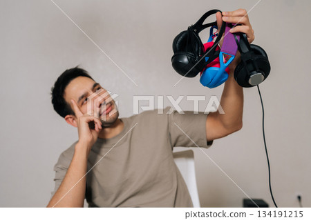 Man considering different models of headphones, holding three diverse pairs while making decision about which audio device to select for listening needs. Contemplating features and sound quality. Man considering different models of headphones, holding three diverse pairs while making decision about which audio device to select for listening needs. Contemplating features and sound quality. 134191215