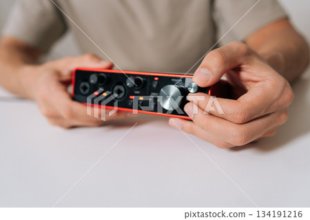 Hands of audio engineer working with audio interface, adjusting device settings to record sound, connecting music equipment, creating professional audio, producing tracks in modern home studio. 134191216