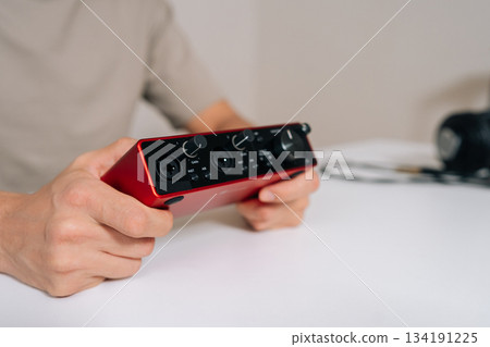 Close-up of sound engineer or musician holding compact red audio interface, crucial piece of equipment for recording and producing music with superior audio quality in modern home studio setup. 134191225