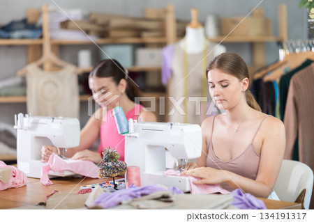 Adult and young women seamstresses sewing on machine Adult and young women seamstresses sewing on machine 134191317