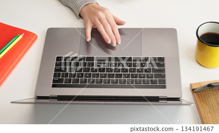 Close-up of a female hand on a laptop touchpad at a white desk, top view. Remote education, research, browsing, internet search. Close-up of a female hand on a laptop touchpad at a white desk, top view. Remote education, research, browsing, internet search. 134191467