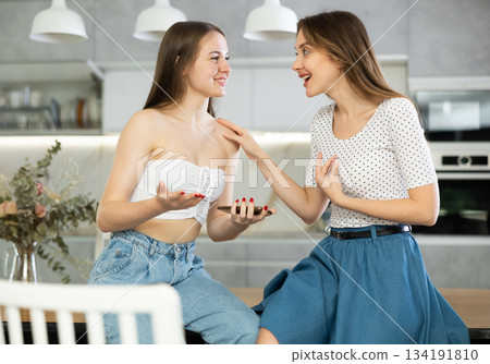Two young women talking while sitting on table in kitchen 134191810