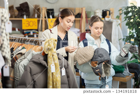 Discontented teen girl with mother choosing hat in clothing store 134191818