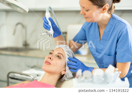 Adult woman cosmetologist doing moisturizing procedure to young woman 134191822