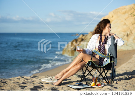 Relaxed half-dressed businesswoman savoring whiskey on seashore Relaxed half-dressed businesswoman savoring whiskey on seashore 134191829