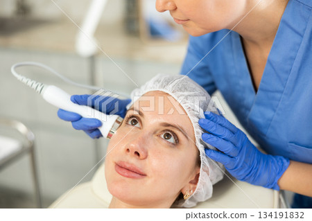 Adult woman cosmetologist doing ultrasound procedure to young woman 134191832