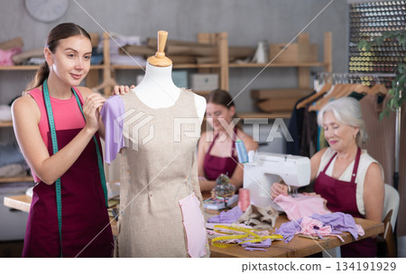 Mature head of manufacturing and girl assistant sewing, female designer work with mannequin. Mature head of manufacturing and girl assistant sewing, female designer work with mannequin. 134191929