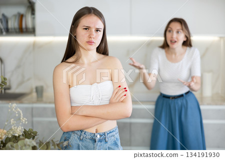 Offended young girl standing in the kitchen, angry mother talking Offended young girl standing in the kitchen, angry mother talking 134191930