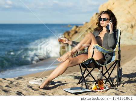 Tempting businesswoman drinking whiskey and talking on phone on beach Tempting businesswoman drinking whiskey and talking on phone on beach 134191961