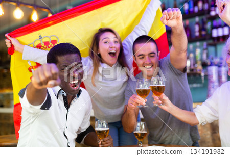 Spanish male and female soccer football fans celebrating championship win, waving flag of Spain in pub Spanish male and female soccer football fans celebrating championship win, waving flag of Spain in pub 134191982