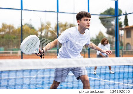 Young European male player serving ball during training padel in court outdoors in spring Young European male player serving ball during training padel in court outdoors in spring 134192090