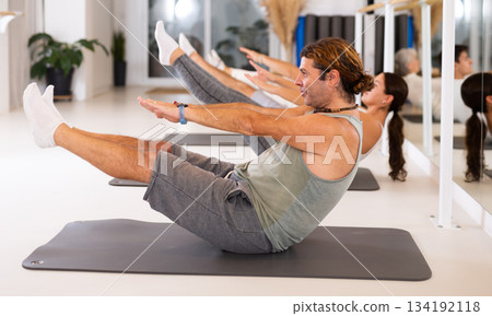 Active vigorous man performs exercises on a pilates mat in the hall of a modern fitness studio. 134192118