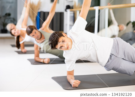 Positive athletic male performing set of exercises on a pilates mat during group class in fitness studio. Positive athletic male performing set of exercises on a pilates mat during group class in fitness studio. 134192120