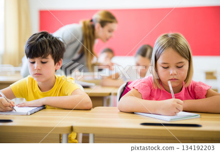 Focused preteen pupils studying in classroom with female teacher 134192203