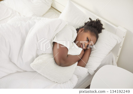 Sad African American woman lying in bed, hugging pillow, feeling bad and unwilling to get up early. 134192249