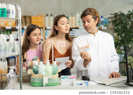Mother and daughter choose pills in drugstore. Male pharmacist offers to buy pills Mother and daughter choose pills in drugstore. Male pharmacist offers to buy pills 134192252