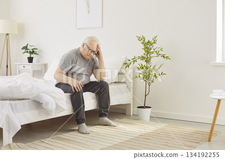 Senior elderly sleepless man suffering from headache sitting on bed in bedroom at home. Senior elderly sleepless man suffering from headache sitting on bed in bedroom at home. 134192255