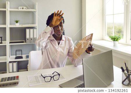 Exhausted woman at her workplace in office suffering from hot weather and lack of air conditioning. 134192261