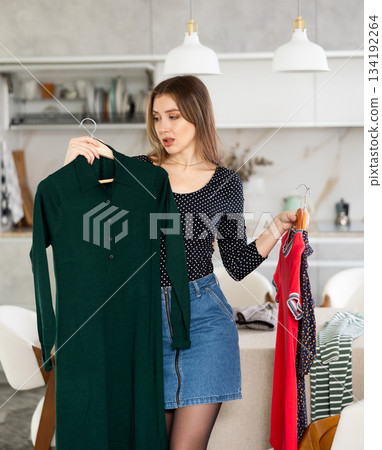 Young upset woman choosing which dress to wear 134192264
