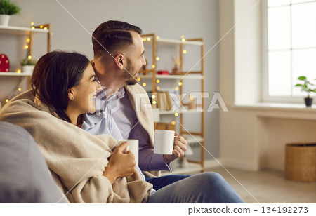 Couple sitting on sofa in the living room at home with a cup of tea or coffee and laughing. 134192273