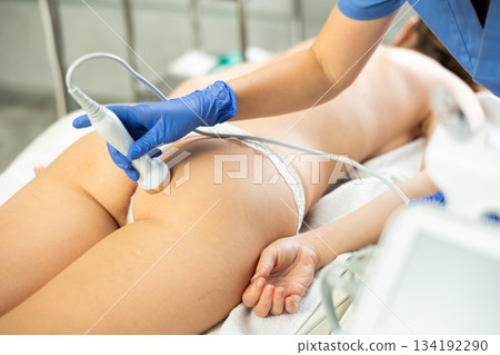 Young woman getting ultrasound cavitation body contouring treatment, anti-cellulite therapy, massage and and moisturizing bottom layer of skin from female cosmetologist. Hardware cosmetology for body Young woman getting ultrasound cavitation body contouring treatment, anti-cellulite therapy, massage and and moisturizing bottom layer of skin from female cosmetologist. Hardware cosmetology for body 134192290