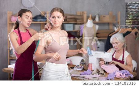 adult female dressmaker takes measurements for a client in the workshop adult female dressmaker takes measurements for a client in the workshop 134192316