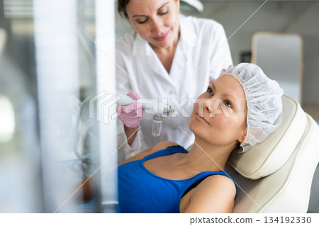 Young female cosmetologist doing moisturizing procedure to adult woman Young female cosmetologist doing moisturizing procedure to adult woman 134192330