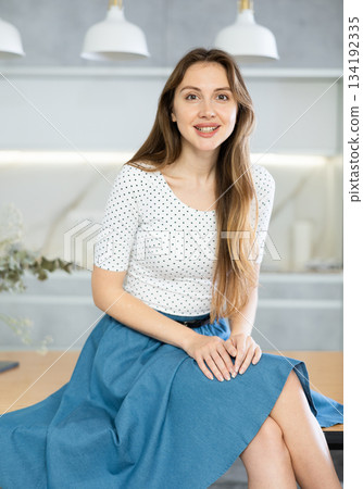 Joyful woman in fashionable clothes and skirt sitting on the kitchen table at home Joyful woman in fashionable clothes and skirt sitting on the kitchen table at home 134192335