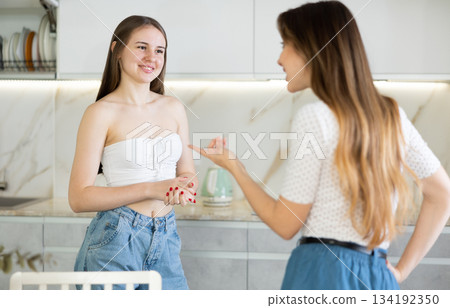 Kind middle-aged mother talking to young daughter in the kitchen Kind middle-aged mother talking to young daughter in the kitchen 134192350