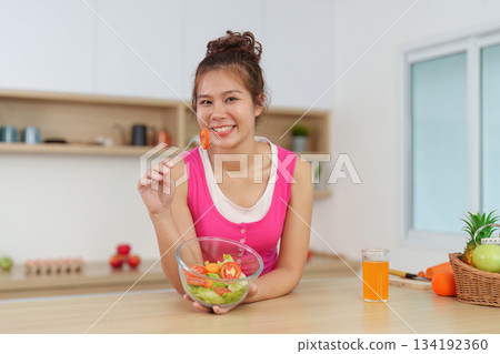 Joyful Eating. Woman smiling while enjoying fresh salad in kitchen. Joyful Eating. Woman smiling while enjoying fresh salad in kitchen. 134192360