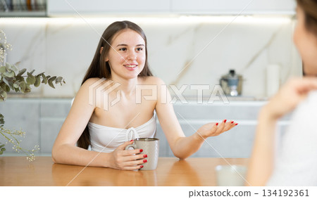 Two young women talking and drinking tea in kitchen Two young women talking and drinking tea in kitchen 134192361