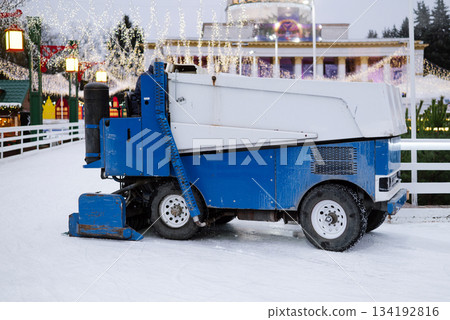 Ice resurfacer machine in blue and white smoothing the surface of an outdoor skating rink decorated 134192816